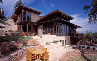 Green Custom Home exterior with stone patio and floor to ceiling windows